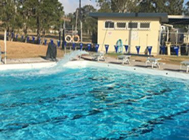 A Large Swimming Pool with A Yellow Building in The Background — Stolzenberg Water Carriers in Chatsworth, QLD