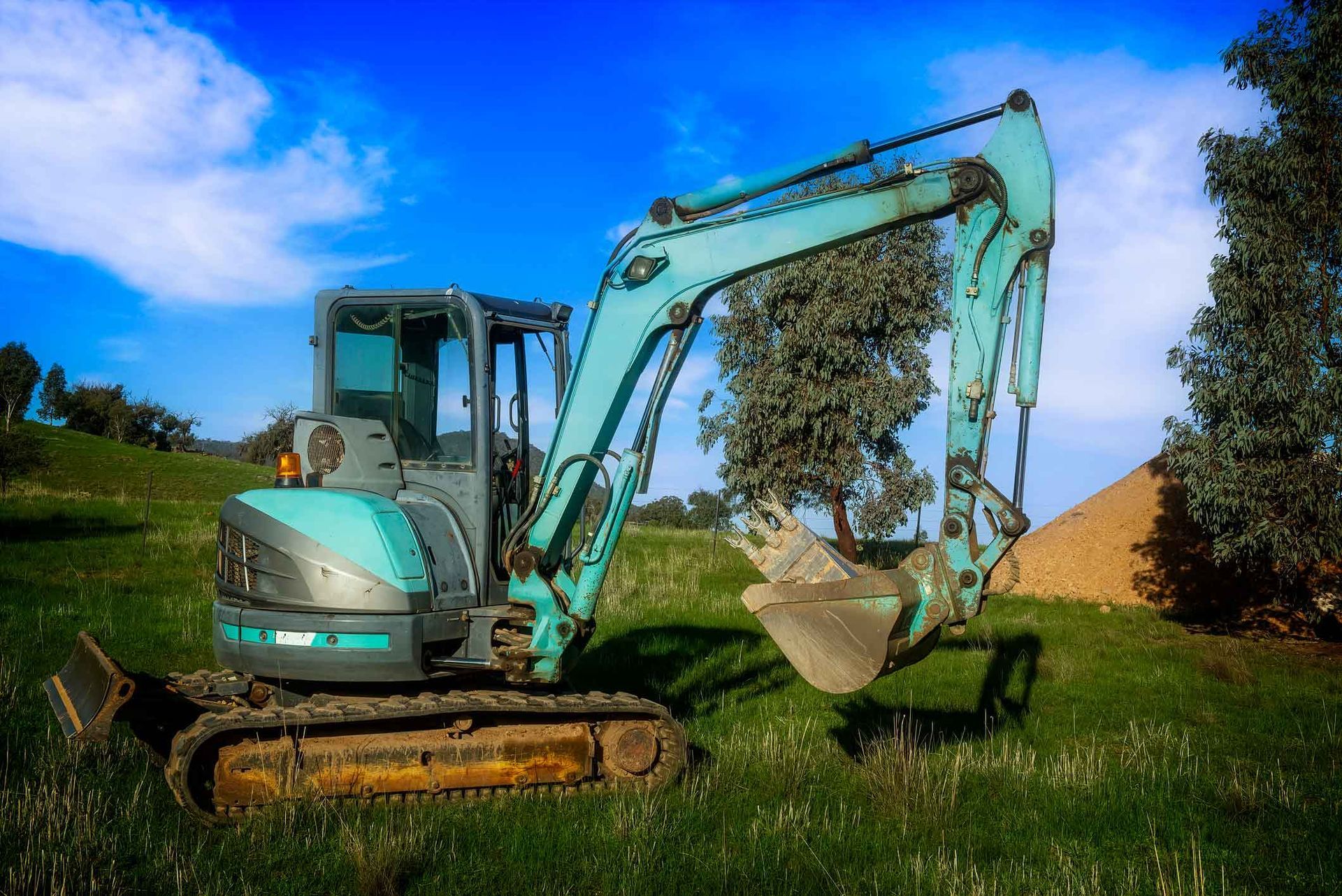 A Small Excavator Is Parked In A Grassy Field – Port Pirie, SA - Flinders Earthmoving & Blue Metal Supplies