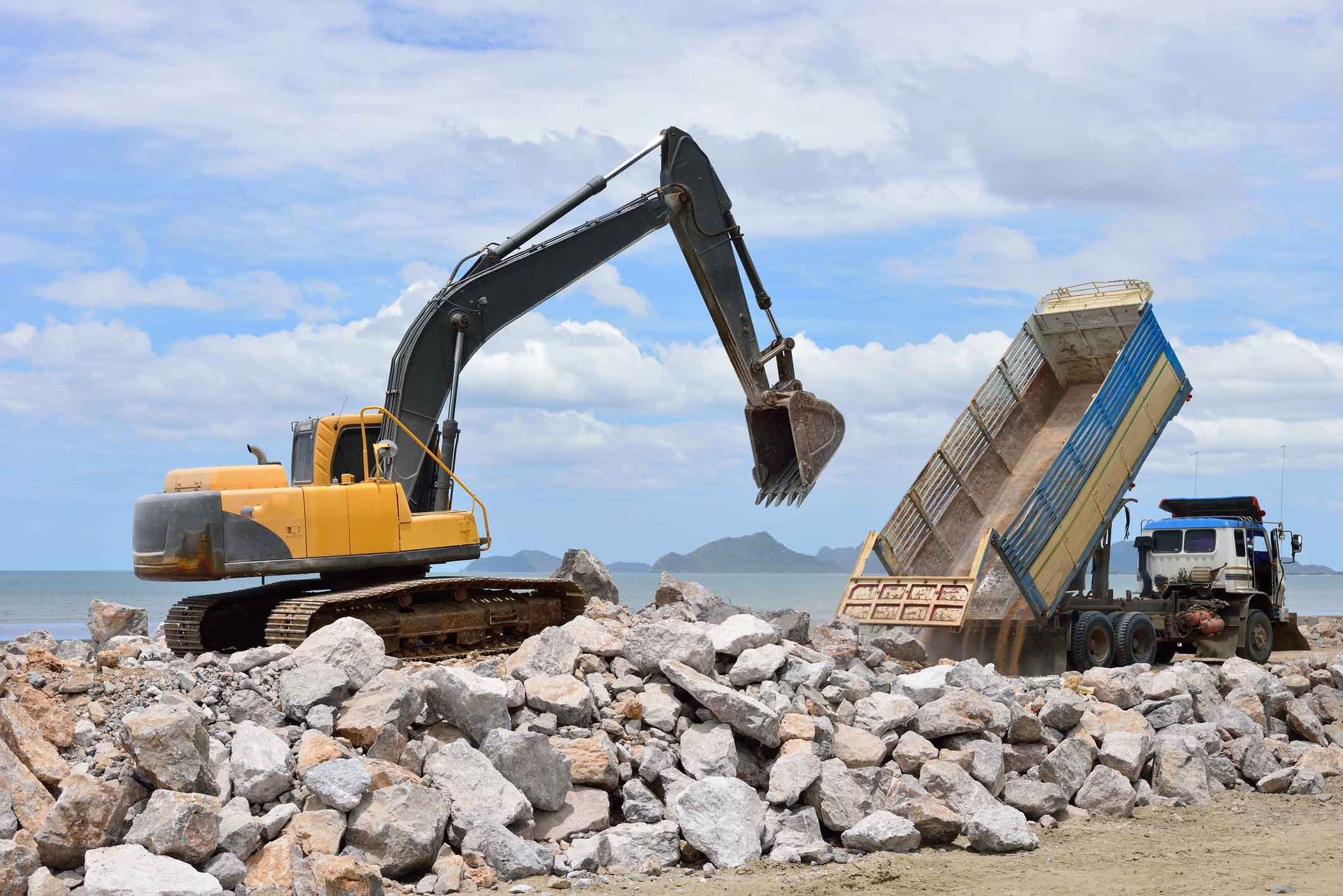 A Yellow Excavator Is Loading Rocks Into A Dump Truck – Port Pirie, SA - Flinders Earthmoving & Blue Metal Supplies