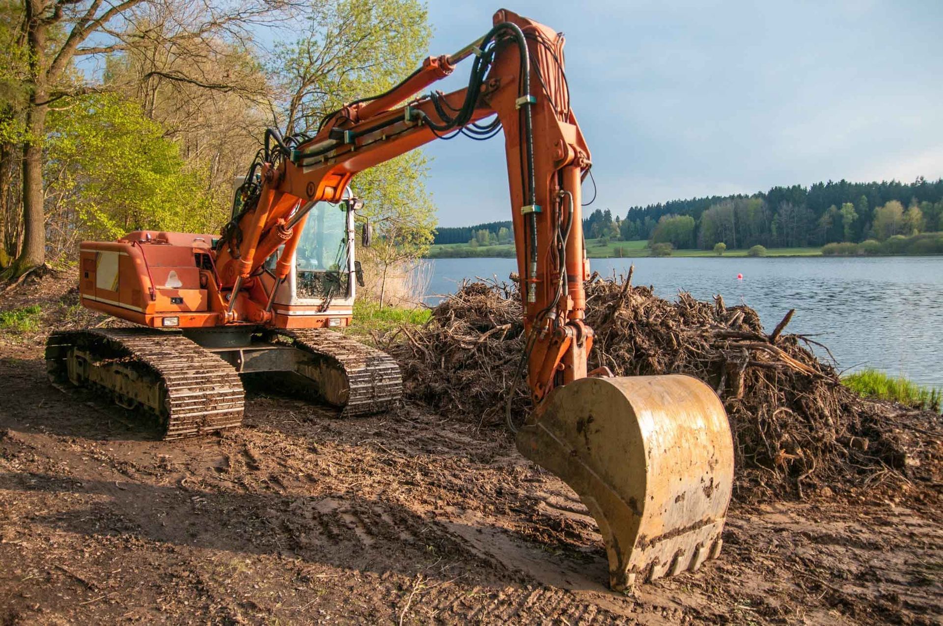 A Large Orange Excavator Is Sitting On Top Of A Pile Of Dirt Next To A Lake – Port Pirie, SA - Flinders Earthmoving & Blue Metal Supplies