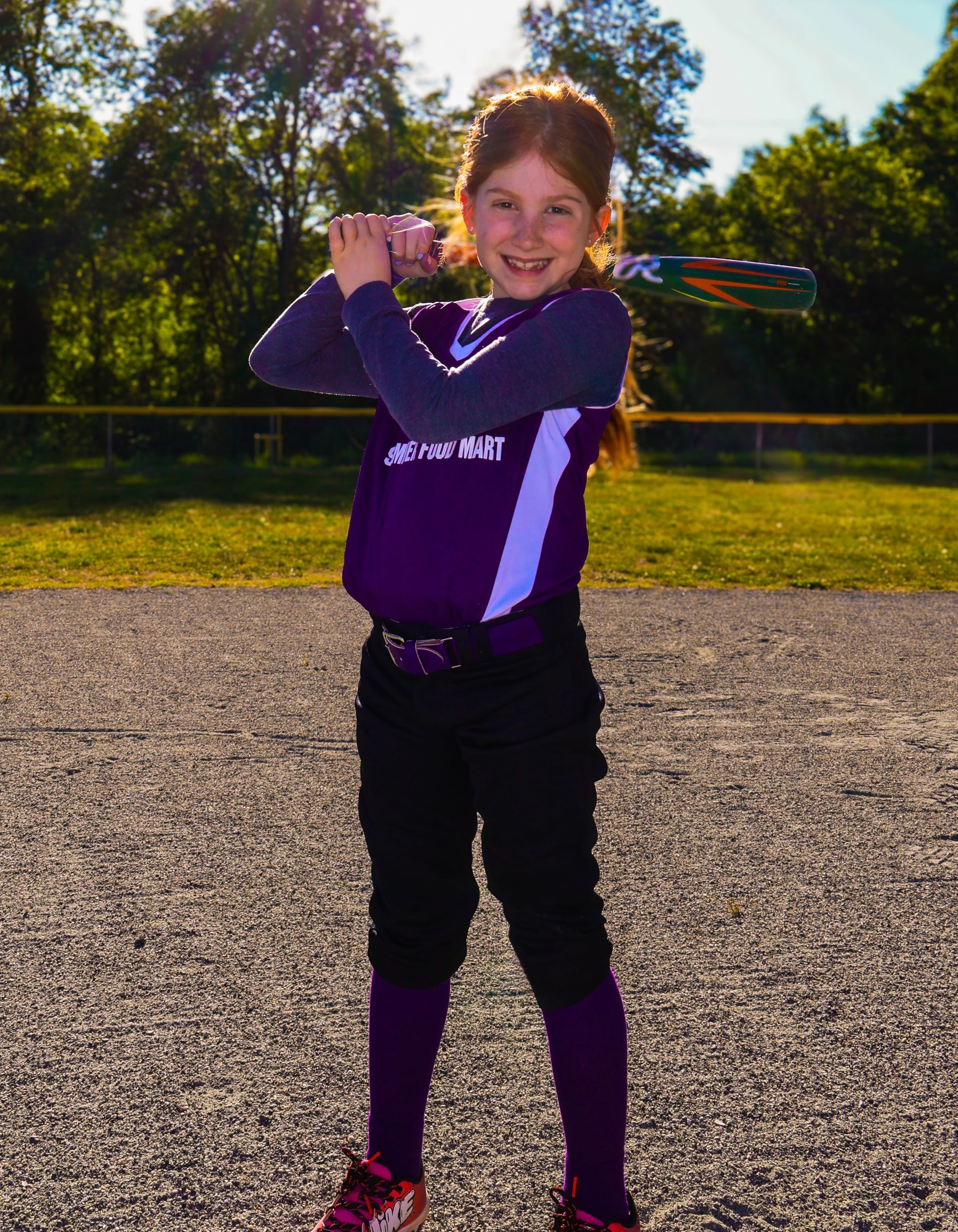 Young baseball player in purple uniform holding a bat on a sunny field