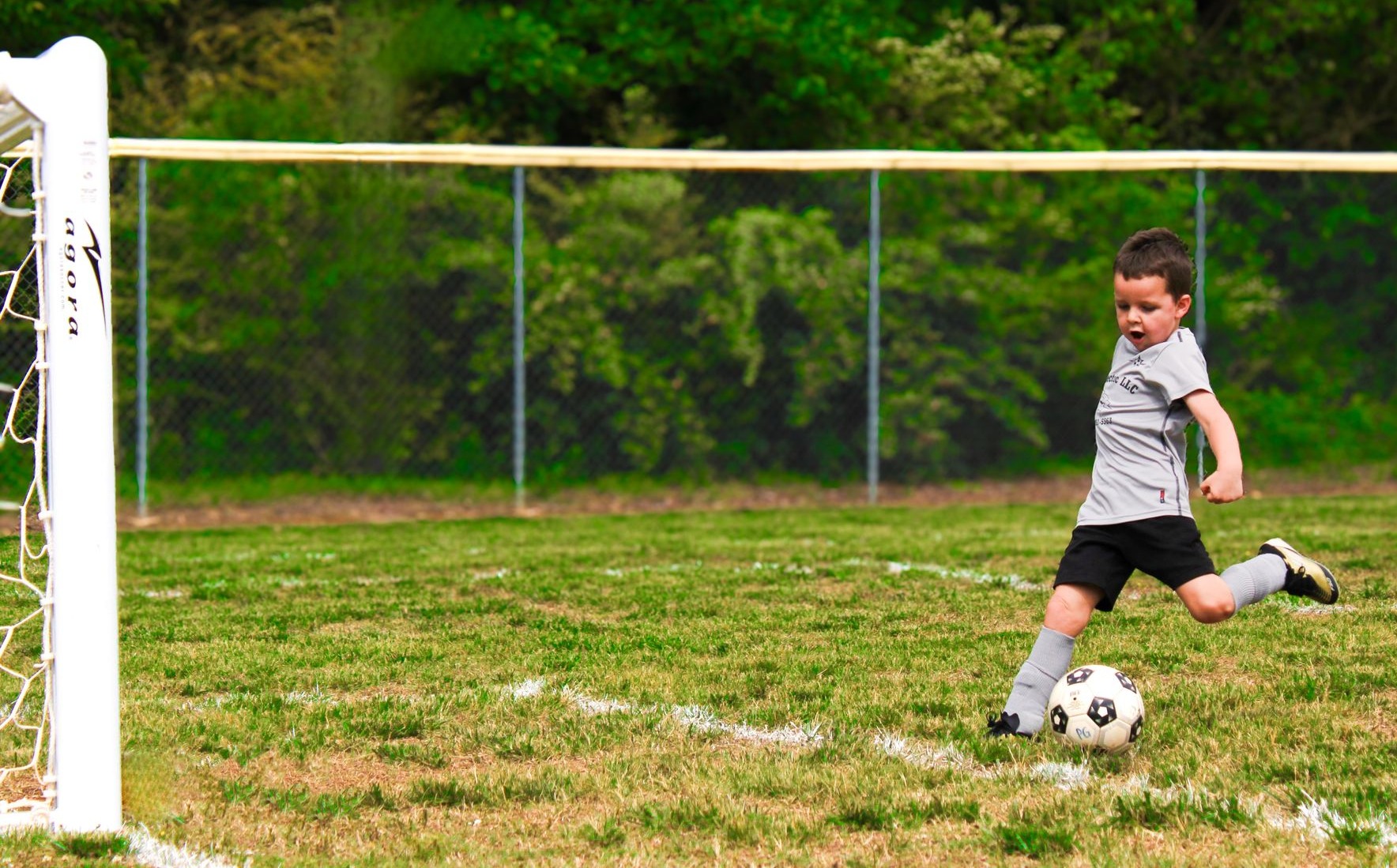 Child kicking a soccer ball toward a goal on a grassy field