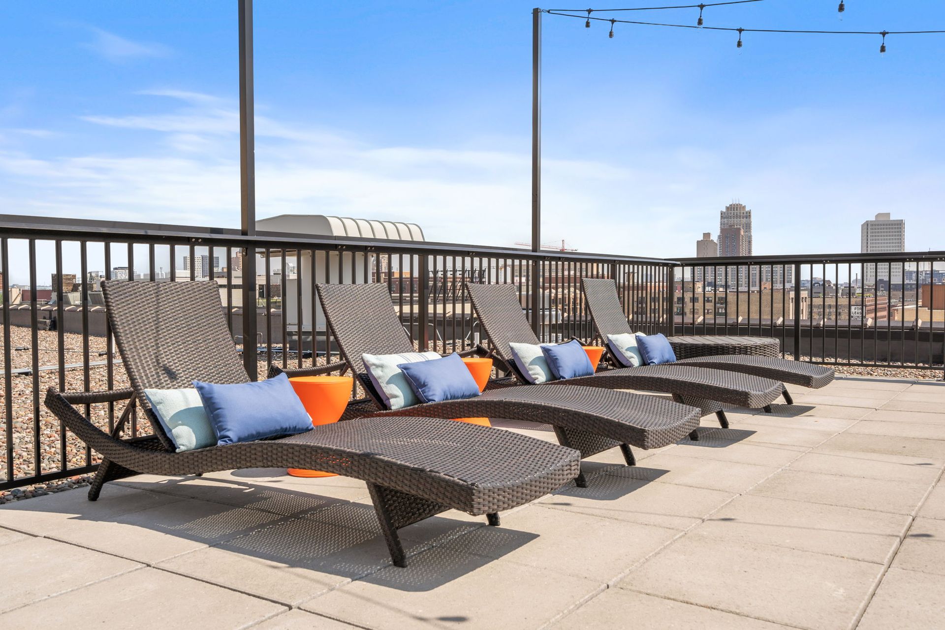 Rooftop deck with four wicker lounge chairs with blue and white pillows, set against a city skyline under a clear sky.