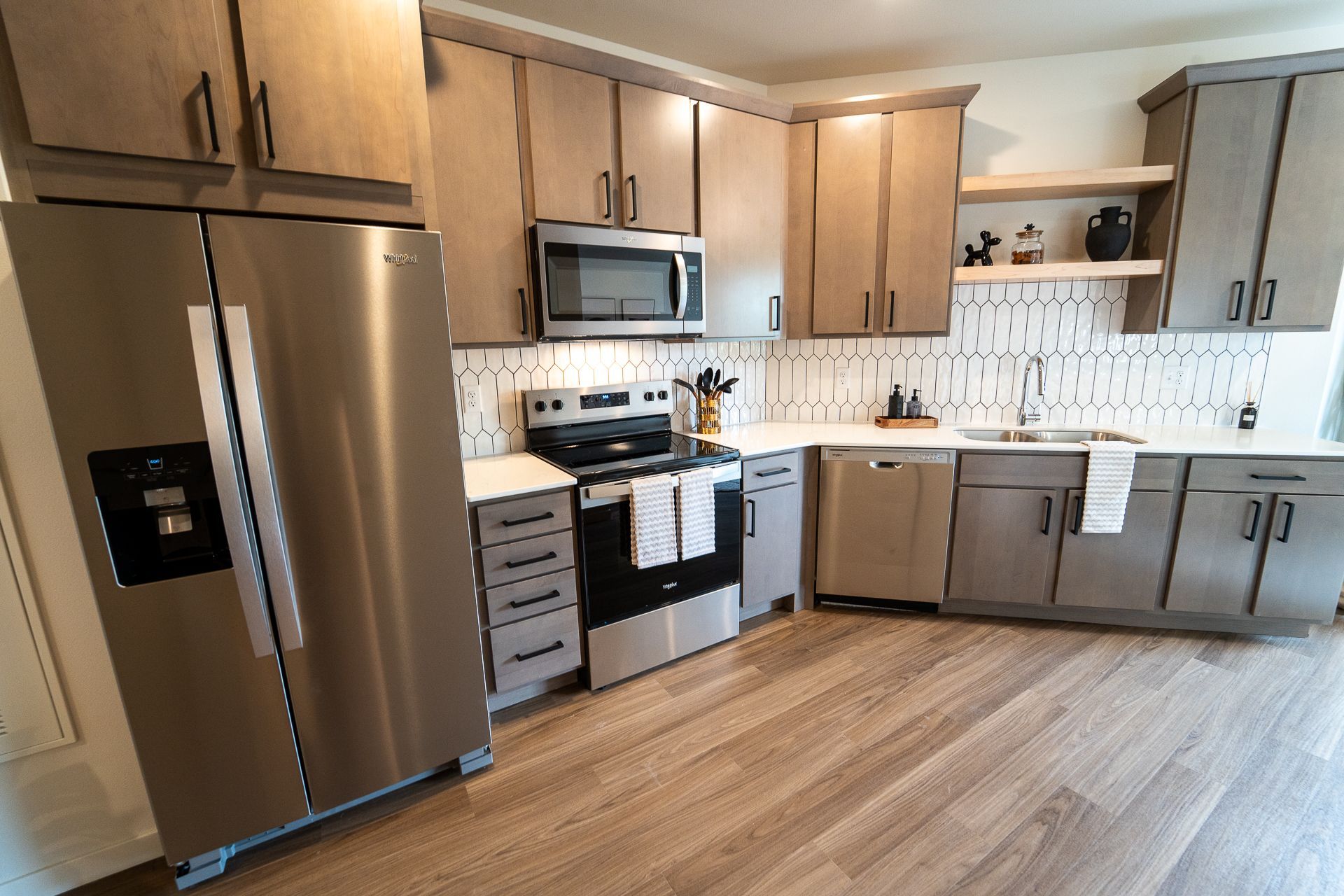 Modern kitchen featuring stainless steel appliances, wood-toned cabinetry, light countertops, and a patterned backsplash.