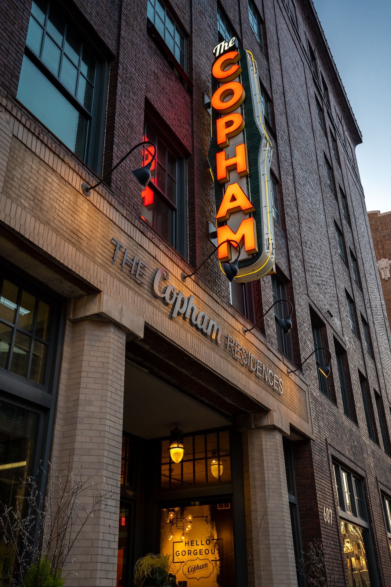 The brick exterior of The Copham building, featuring its vertical illuminated marquee sign against a twilight sky.
