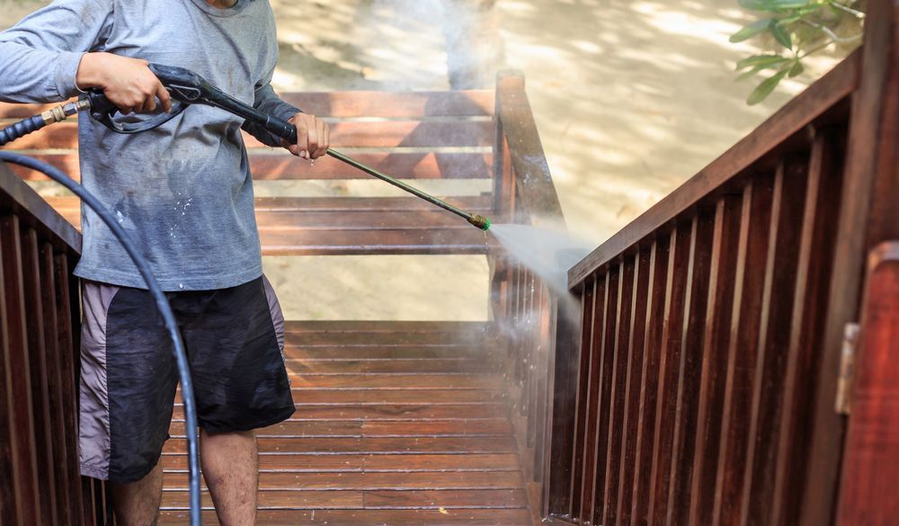 Person power washing wooden stairs outdoors.