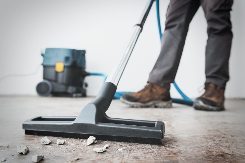 Person using a vacuum cleaner to clean up debris on a floor.