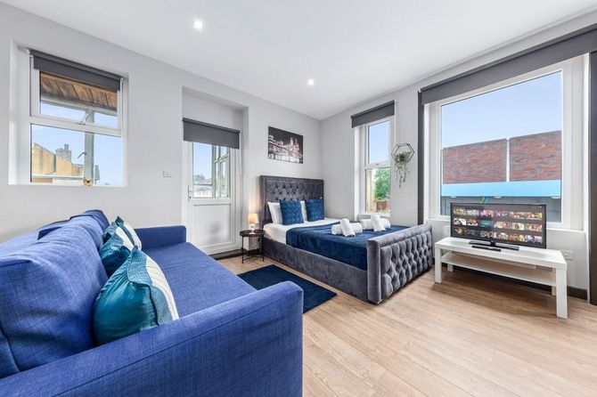 Blue studio apartment with bed, couch, and large windows.