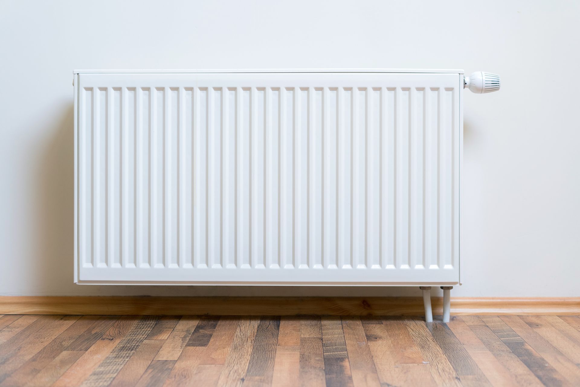 A white radiator is sitting on a wooden floor next to a wall.