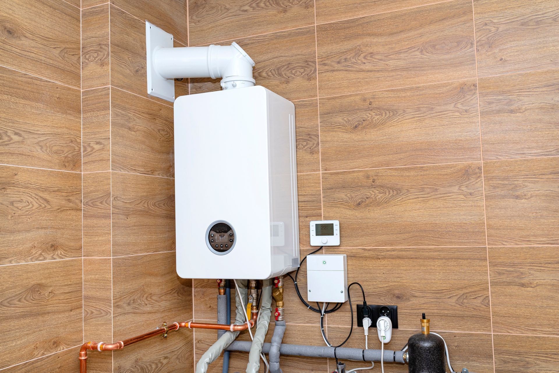 A white boiler is hanging on a wooden wall in a room.