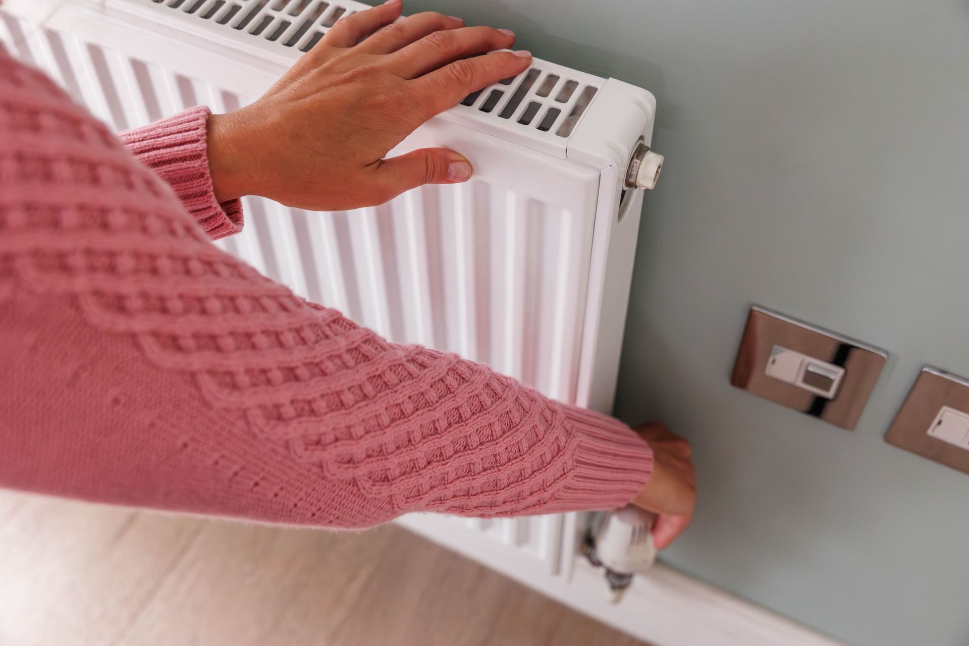 A person in a pink sweater is adjusting a radiator.