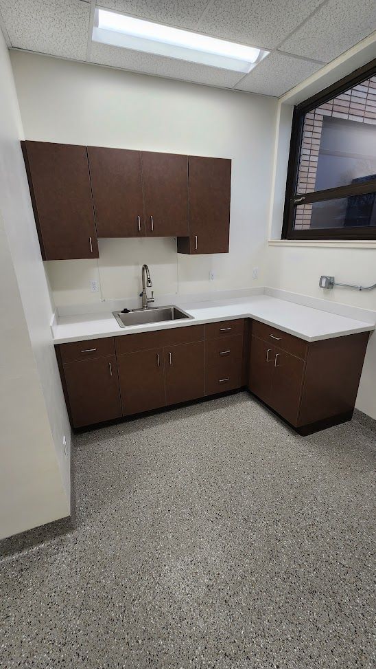 A kitchen with a sink , cabinets , counter tops and a window.