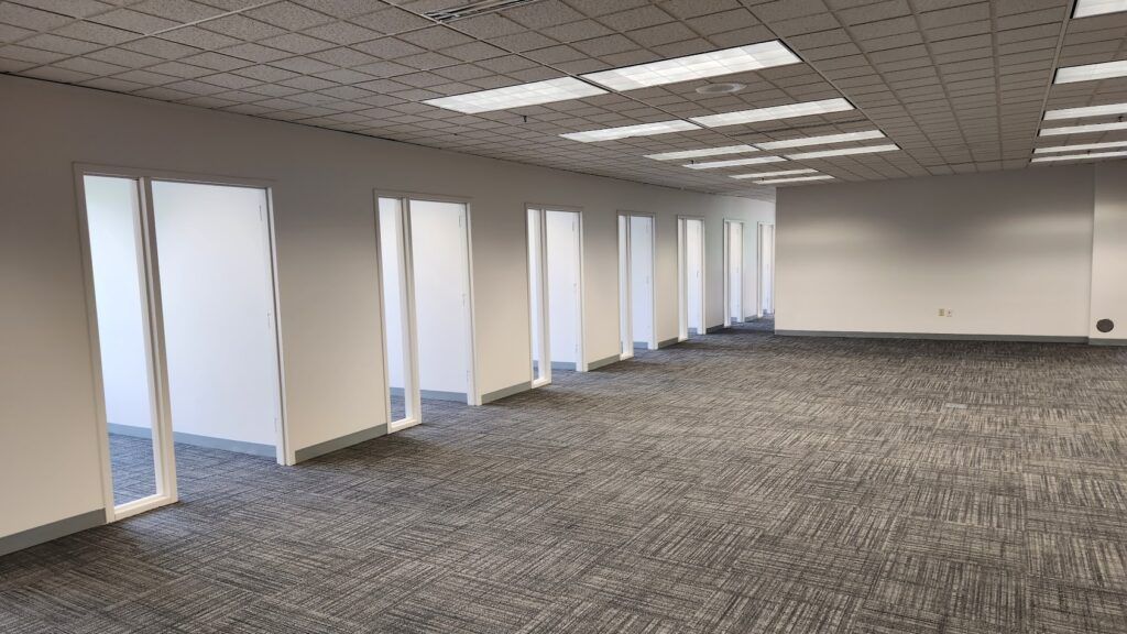 An empty office with a lot of windows and carpeted floors.