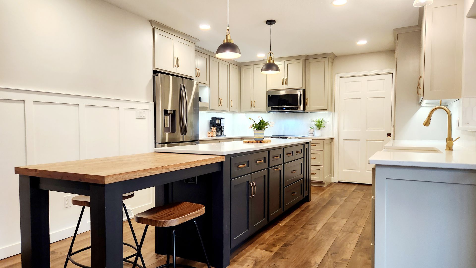 A kitchen with white cabinets , stainless steel appliances , a large island and a wooden table.