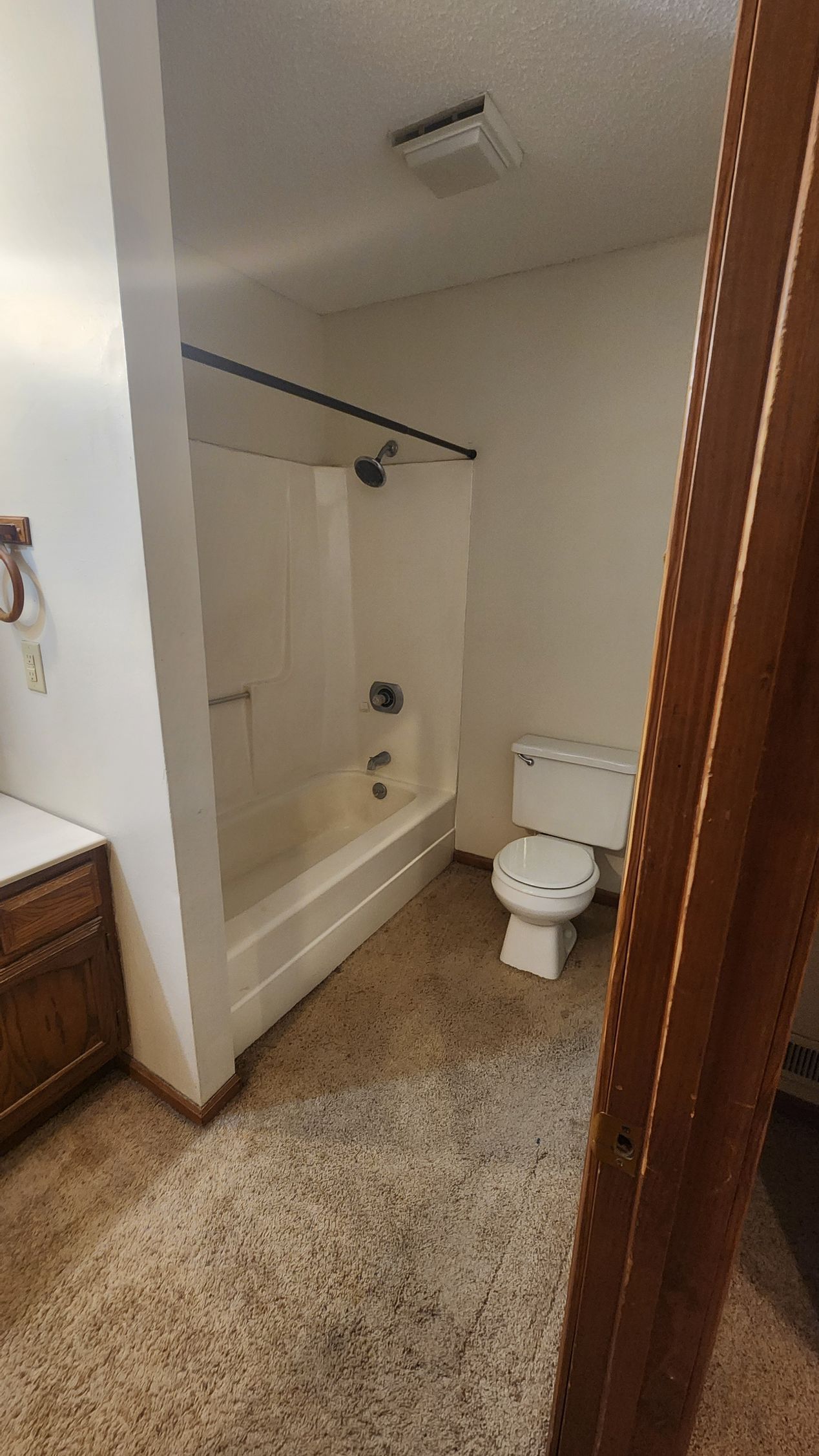 Bathroom with white shower/tub, toilet, brown floor, and wood cabinet.