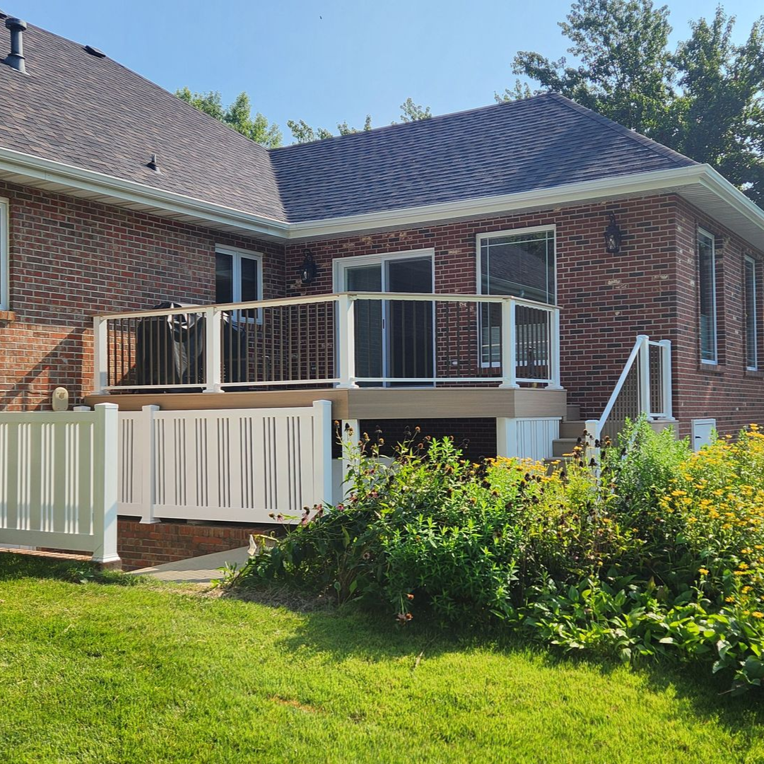 Brick house with a white deck and railing. Green lawn and garden in the foreground.
