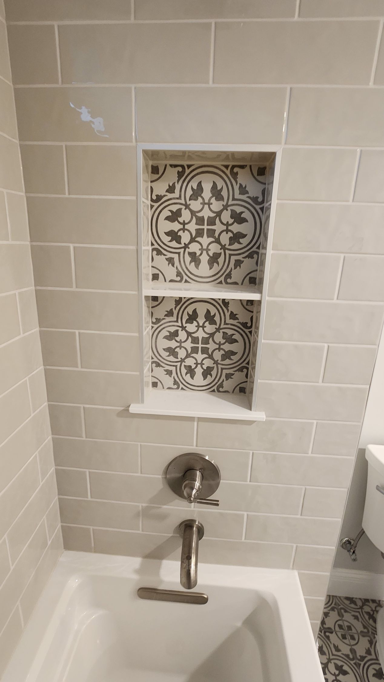 Bathroom with beige tile walls, a decorative tile niche, and a white bathtub.