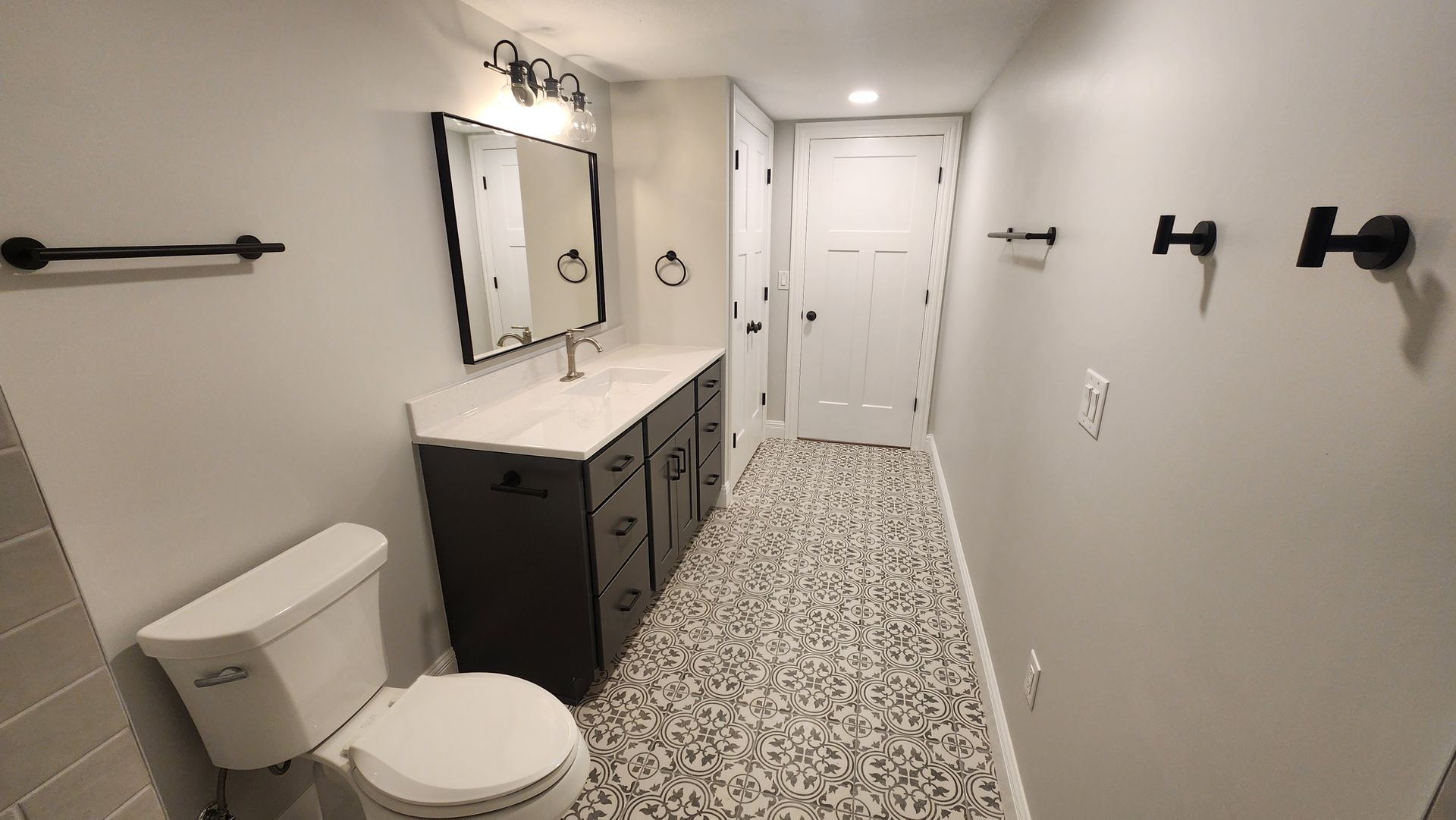 Bathroom with gray walls, vanity, toilet, patterned floor, and black fixtures.