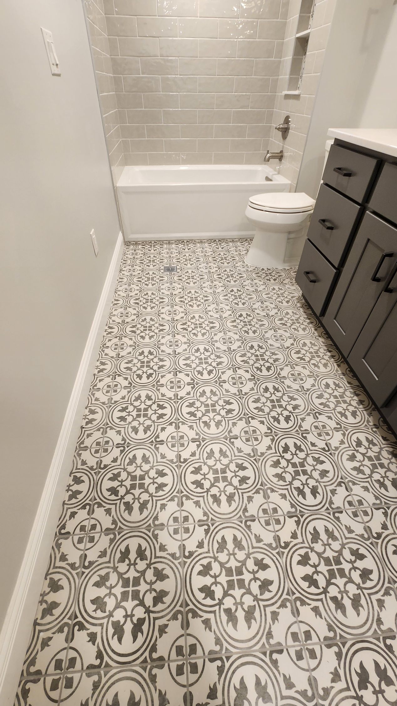 Bathroom with patterned floor tiles, white bathtub, and dark gray vanity.