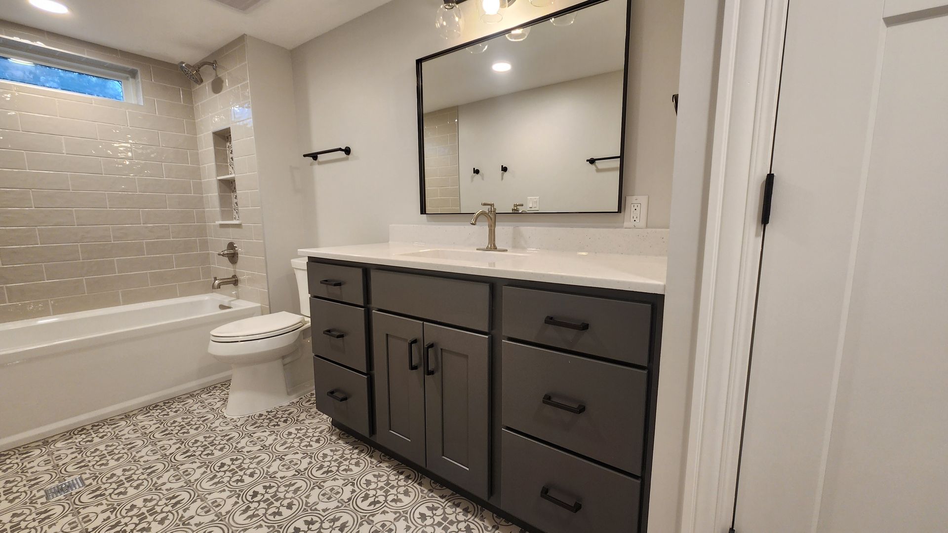 Modern bathroom with gray vanity, patterned floor, and large mirror.