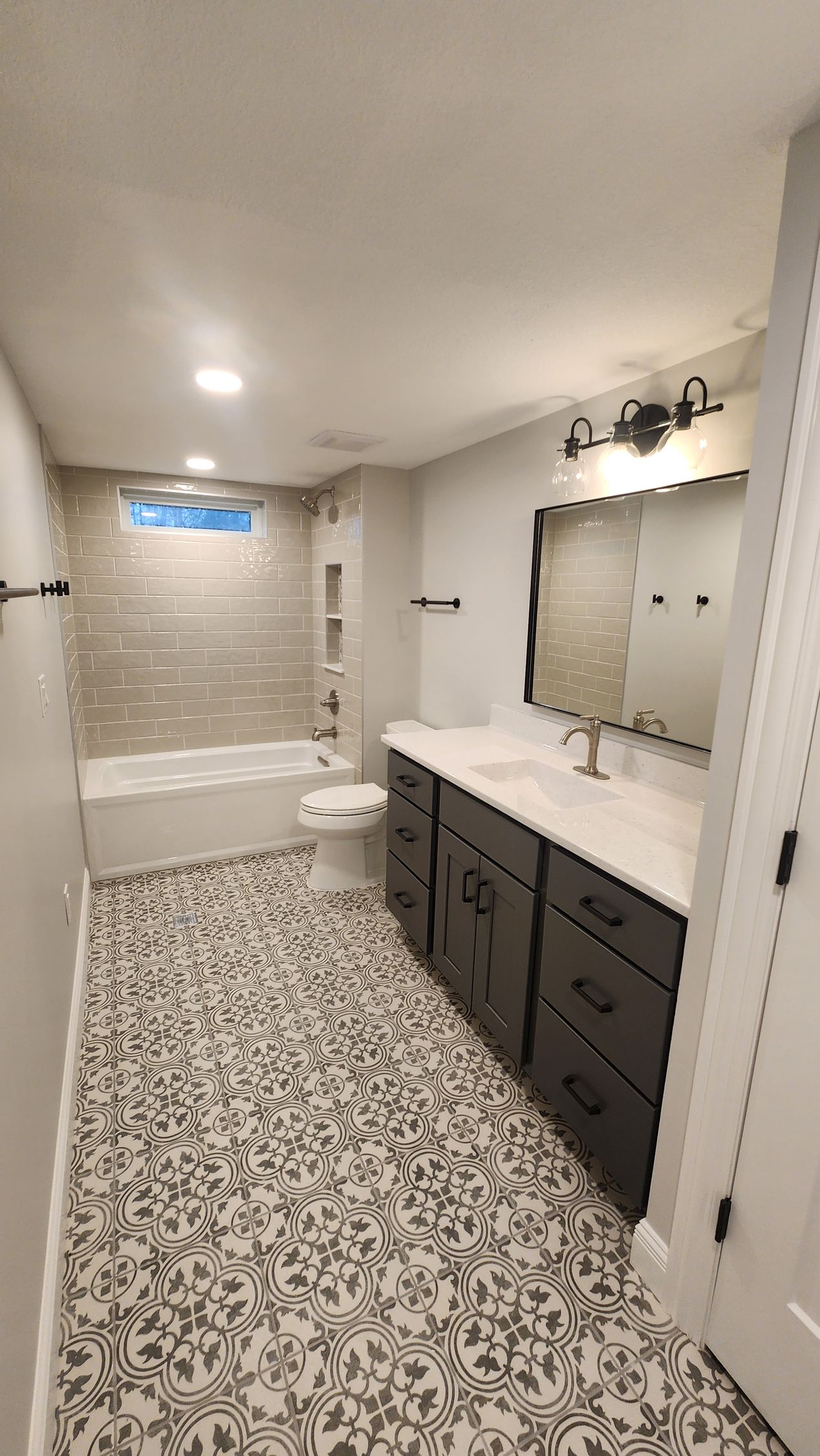 Bathroom with patterned floor, grey walls, dark vanity, and white countertops.