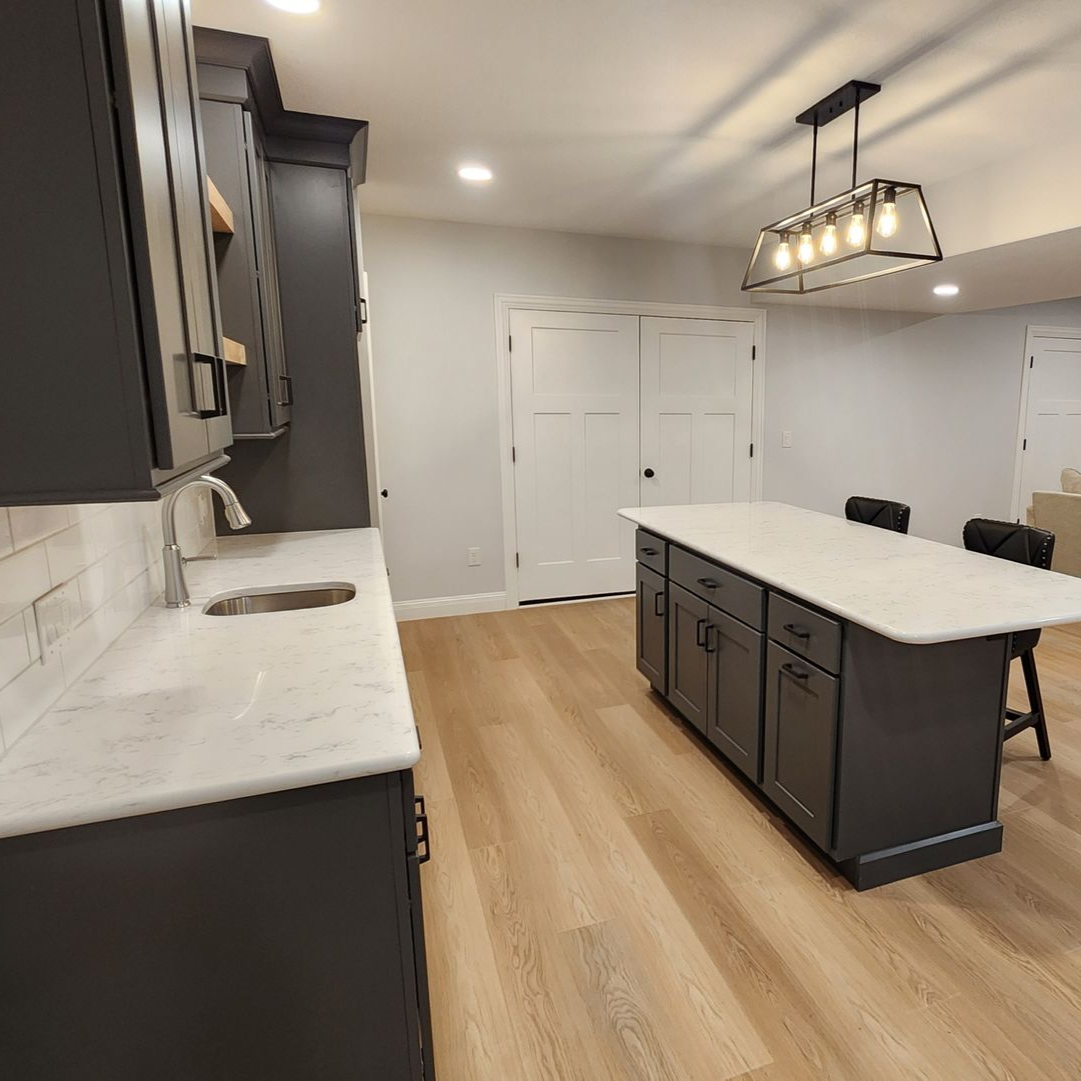Modern kitchen with dark gray cabinets, white countertops, and wooden floors.
