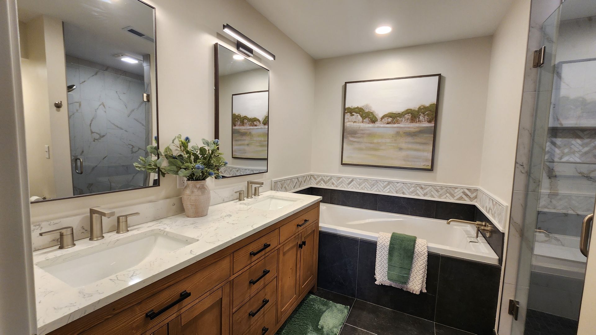 Bathroom with double vanity, tub, and shower. Wood vanity, white countertops, and art.