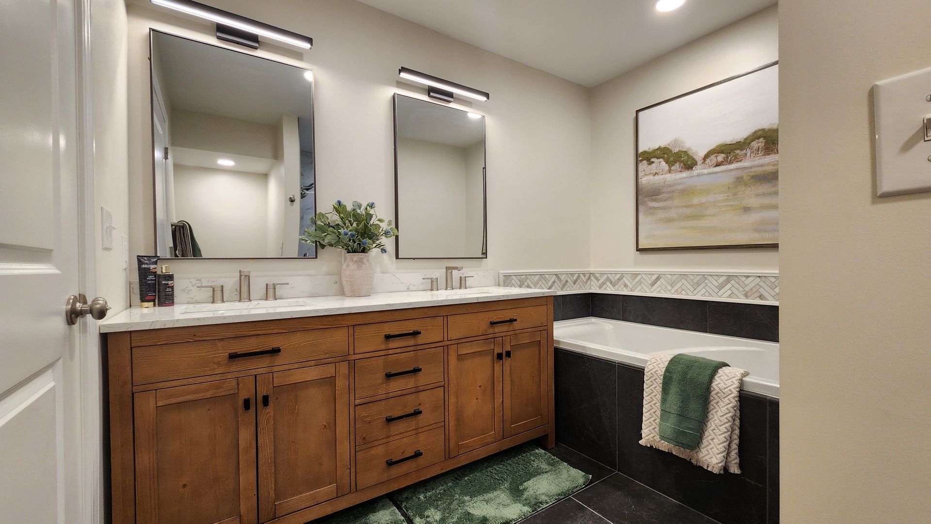 Bathroom with wood vanity, mirrors, tub, and artwork.