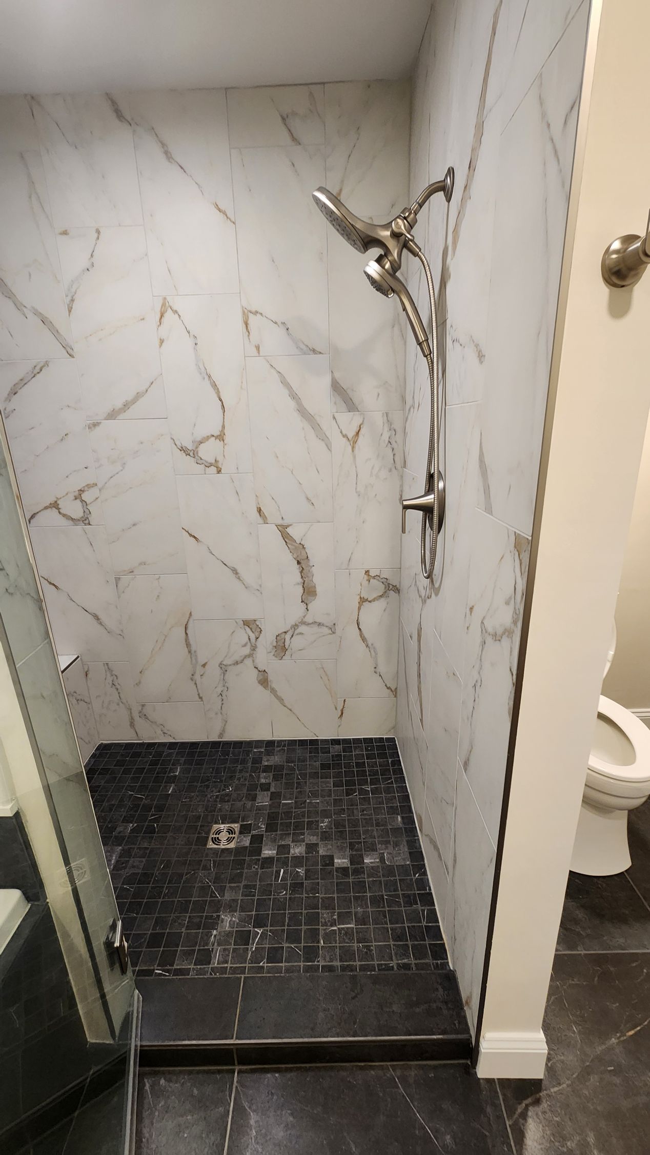 Shower with marble-look walls, black tile floor, and glass door. A toilet is partially visible.