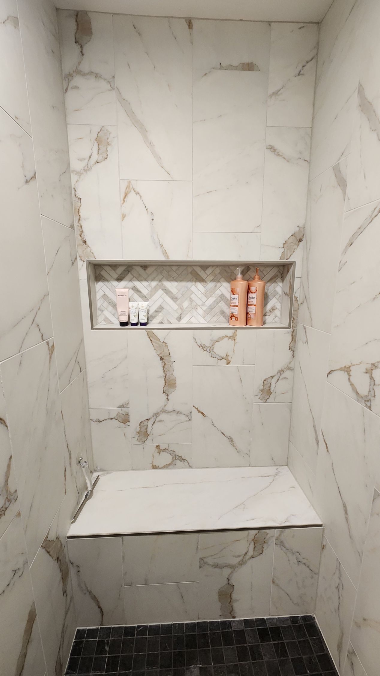 White tiled shower with a built-in shelf and a recessed shelf. Beige and brown accents.