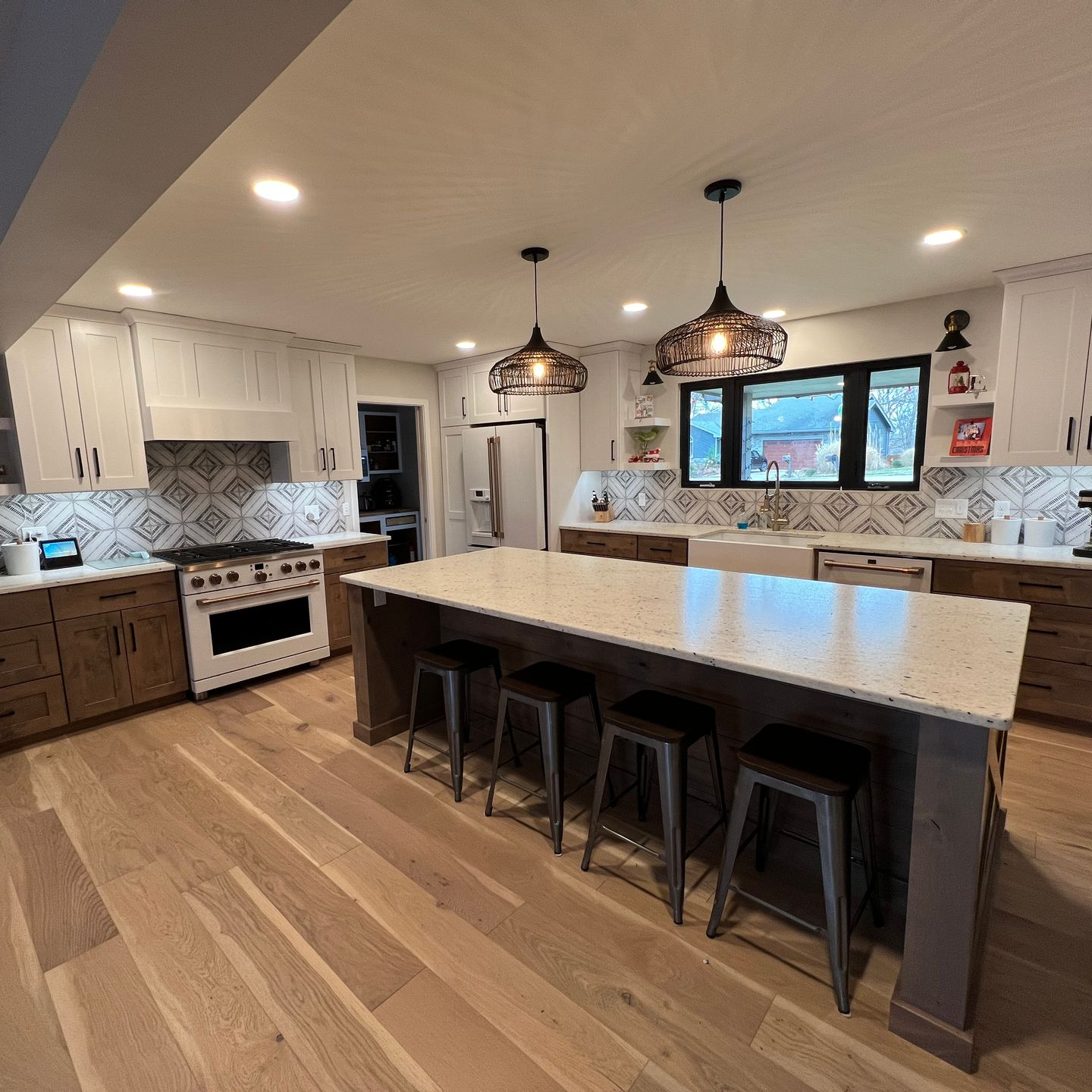 A modern kitchen with a large island, wood floors, white cabinets, and patterned backsplash.