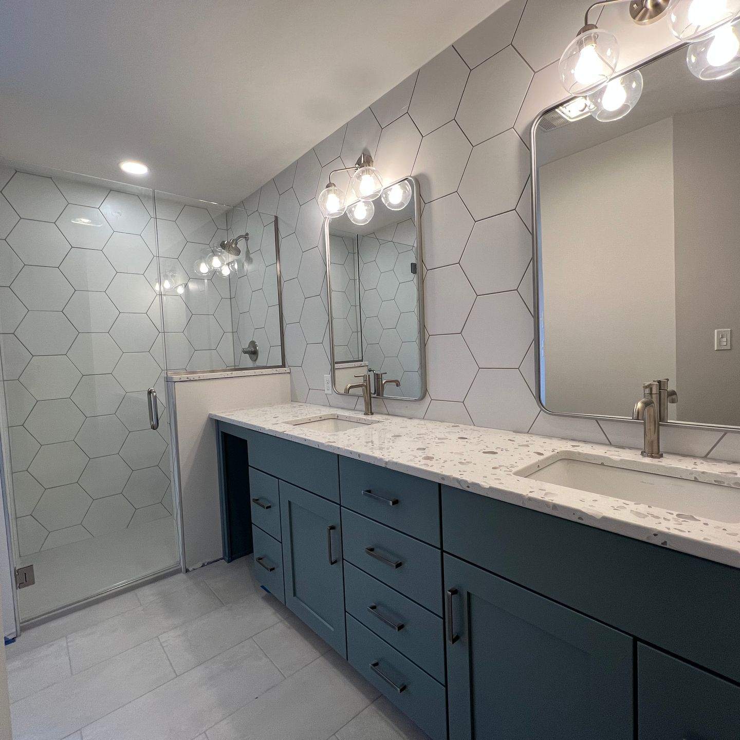 Modern bathroom with blue vanity, white countertops, and hexagonal tile walls.