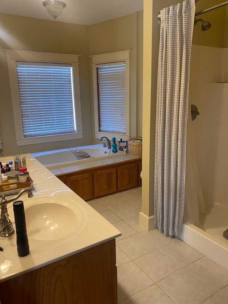 A bathroom with a sink , tub , shower and window.