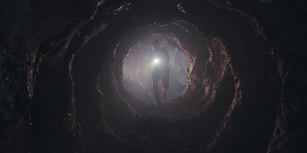 A man is walking through a dark cave with a light at the end.