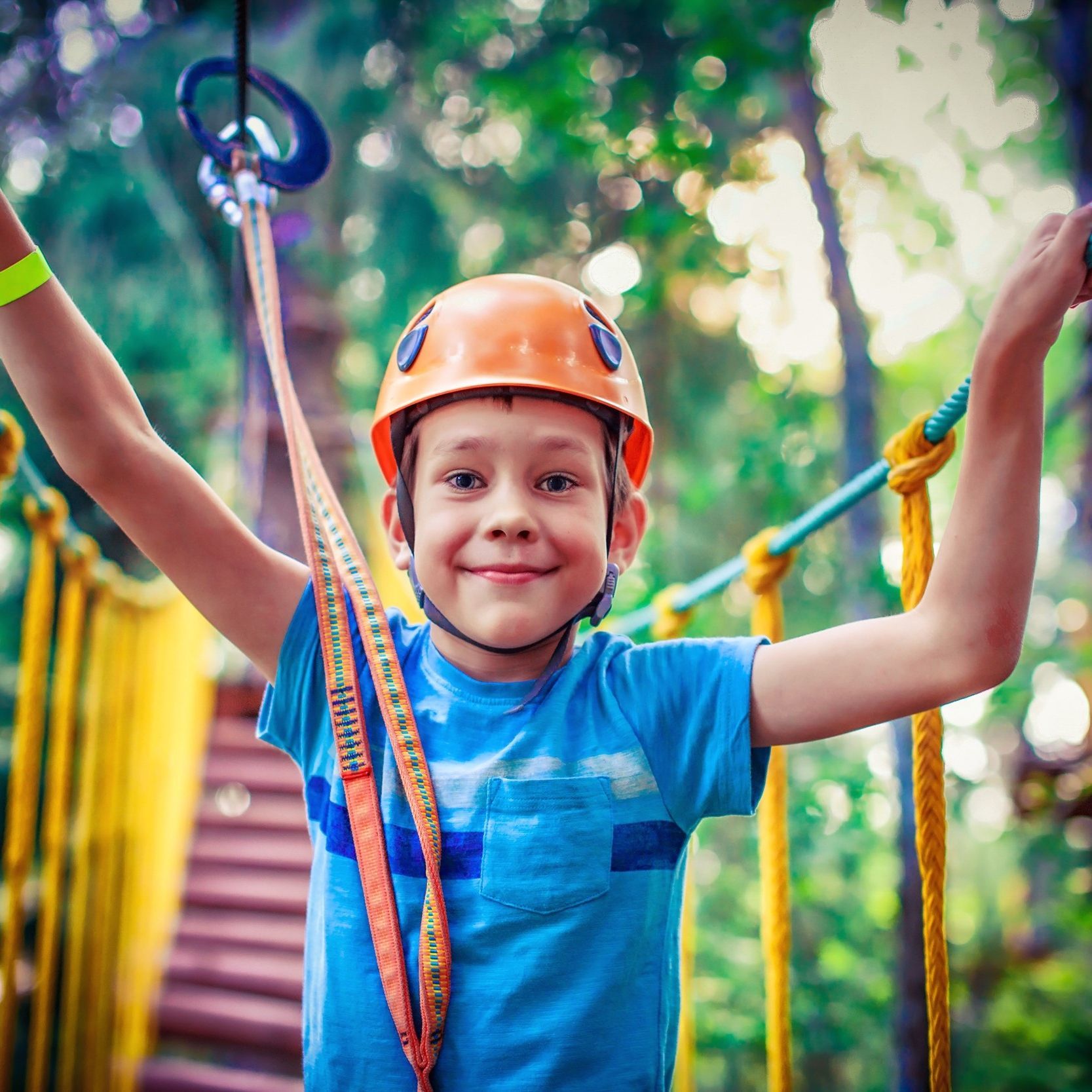 A young boy wearing a blue shirt and an orange helmet is standing on a ropes course.