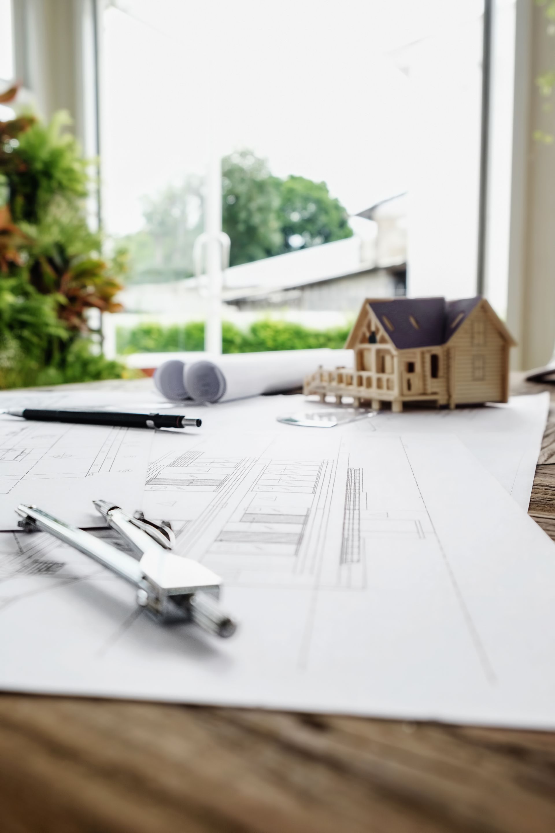 a model house is sitting on top of a table next to a pen and compass .