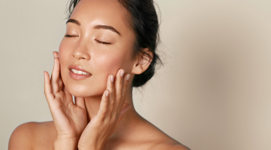 Woman with closed eyes, gently touching her cheeks with both hands, soft lighting.