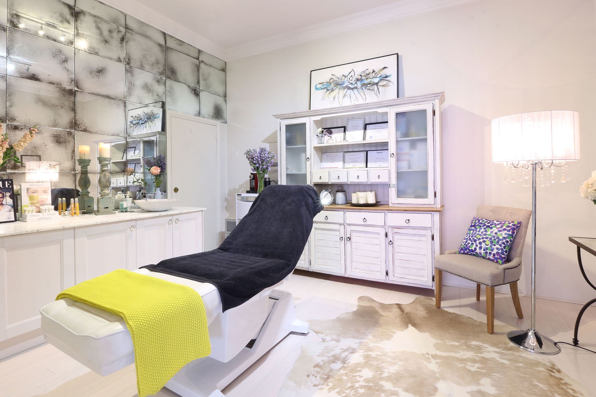 Salon interior: white treatment chair with yellow blanket, white storage, and a floor lamp.