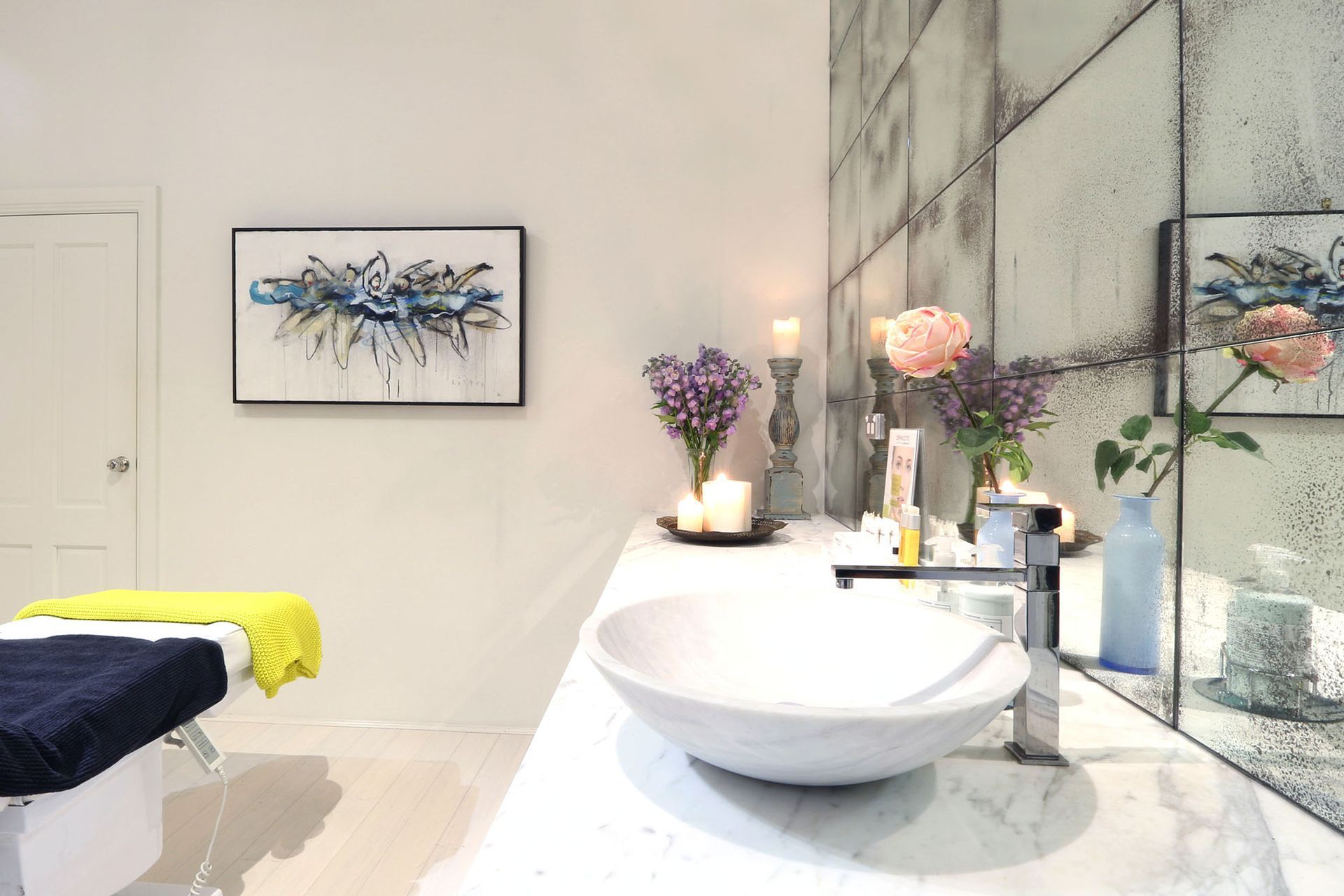 Spa interior with marble countertop, sink, flowers, candles, and artwork. A massage table is on the left.