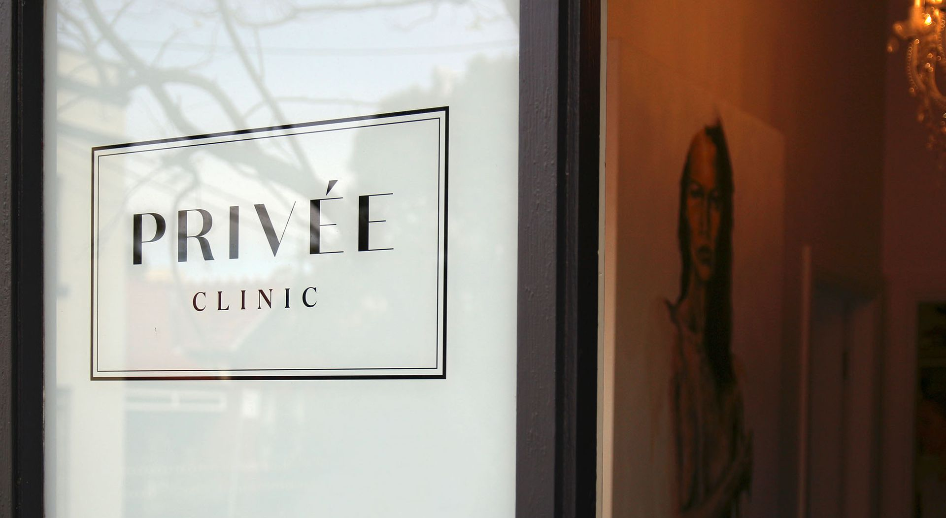 Privee Clinic sign on a glass door. Light shines on a hallway with a portrait.