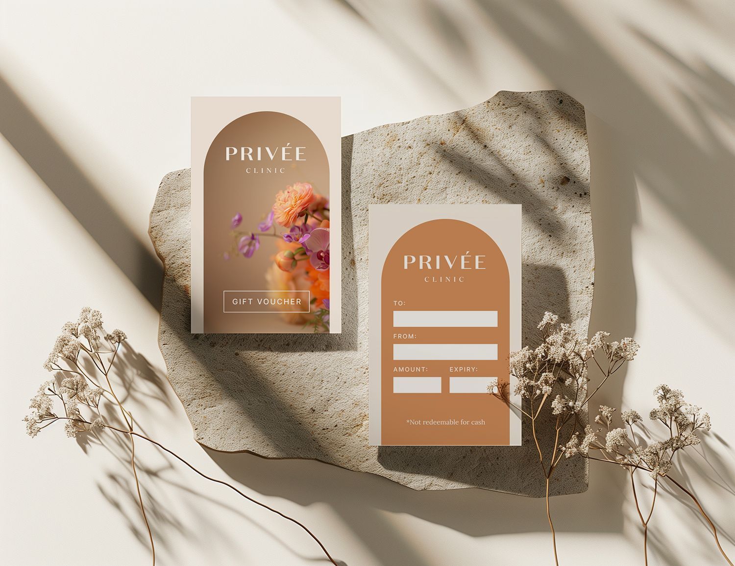 Two business cards with arched tops on a stone, featuring floral design and contact information in earth tones.