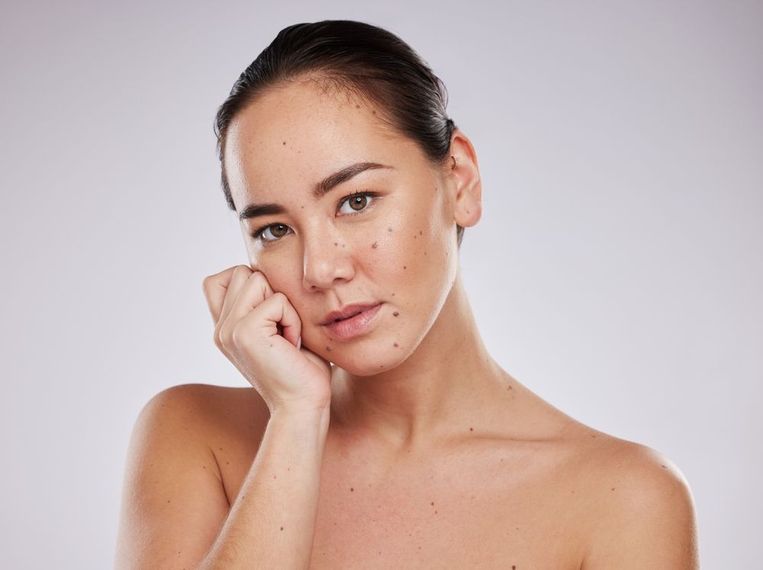 Portrait of a woman with bare shoulders, resting her face on her hand against a light background