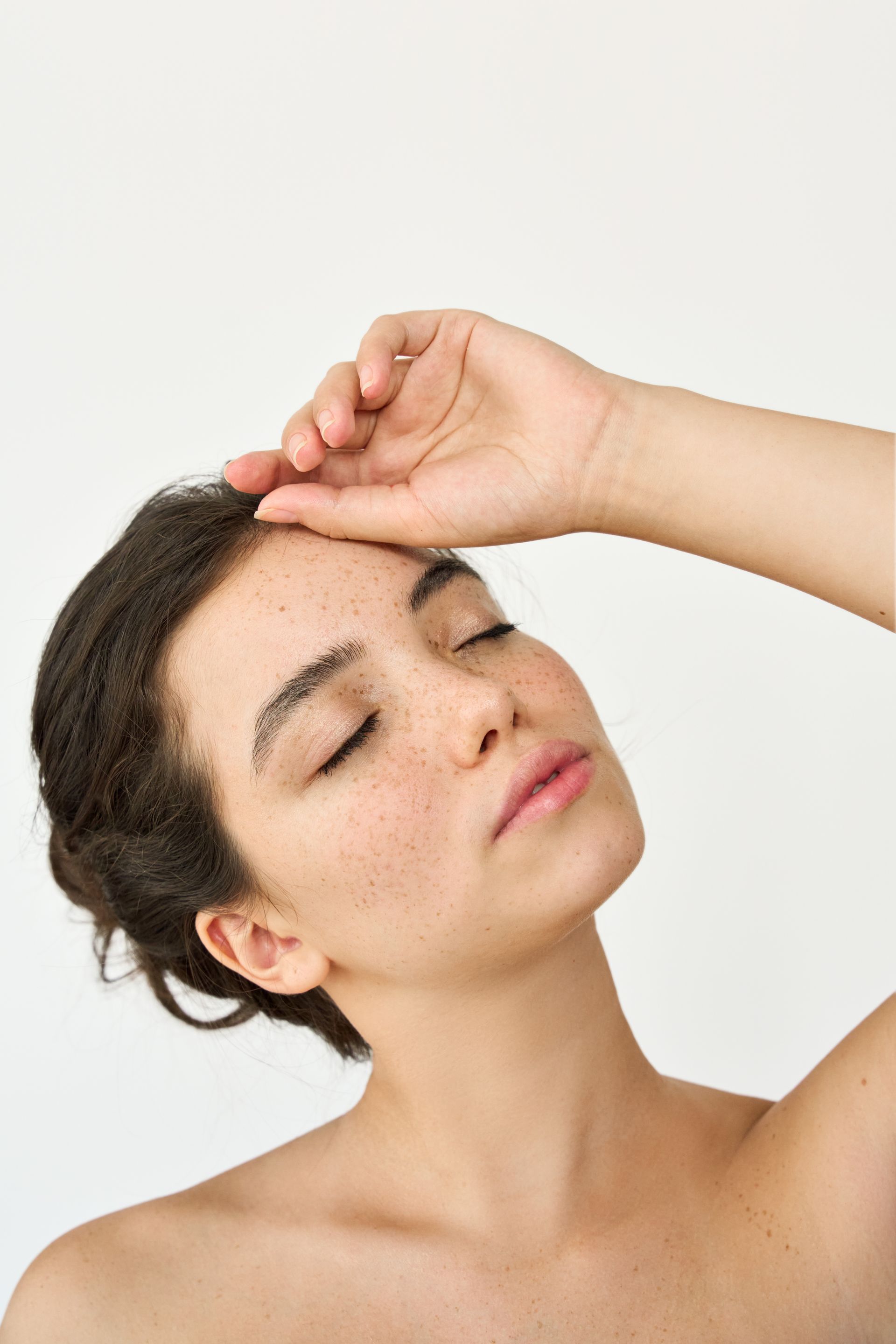 Woman with dark hair in a low bun looking off-camera; wearing a black top, rosy cheeks, natural makeup, and necklace.