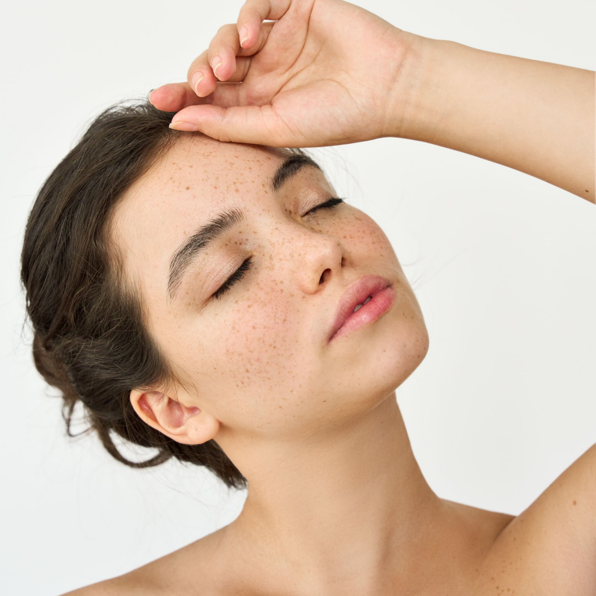 Woman with dark hair in a low bun looking off-camera; wearing a black top, rosy cheeks, natural makeup, and necklace.
