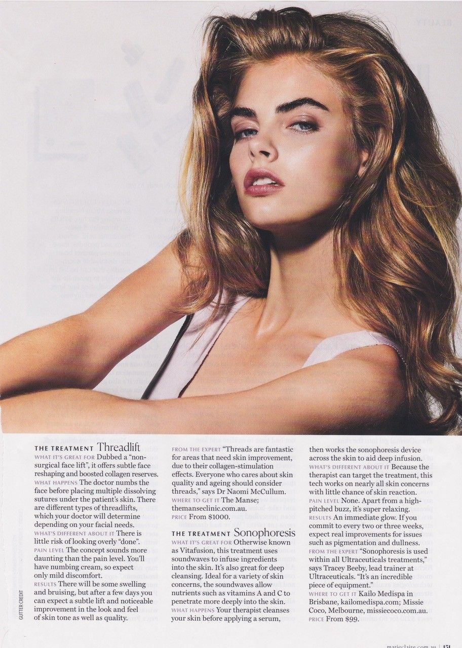 Woman with wavy blonde hair, looking towards the camera. She's wearing a light pink top, soft lighting.