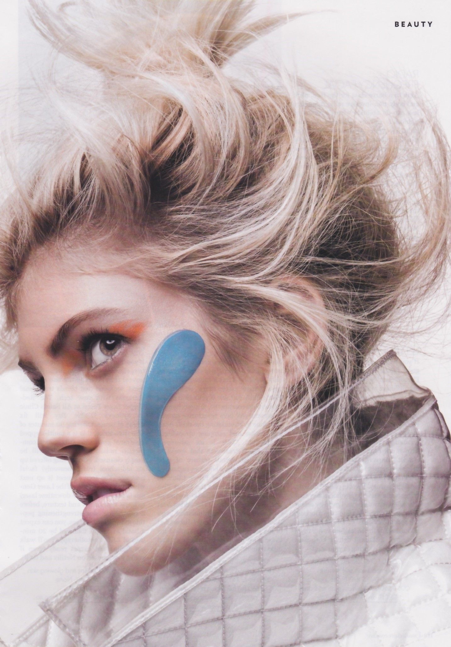 Woman with blonde hair and blue face paint, wearing a quilted jacket, looking off-camera.