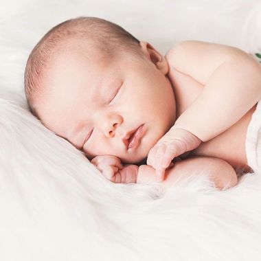 Adorable newborn baby napping on white blanket with arms up