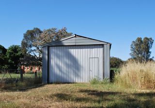 Metal shed in a grassy field with a blue sky and trees in the background.