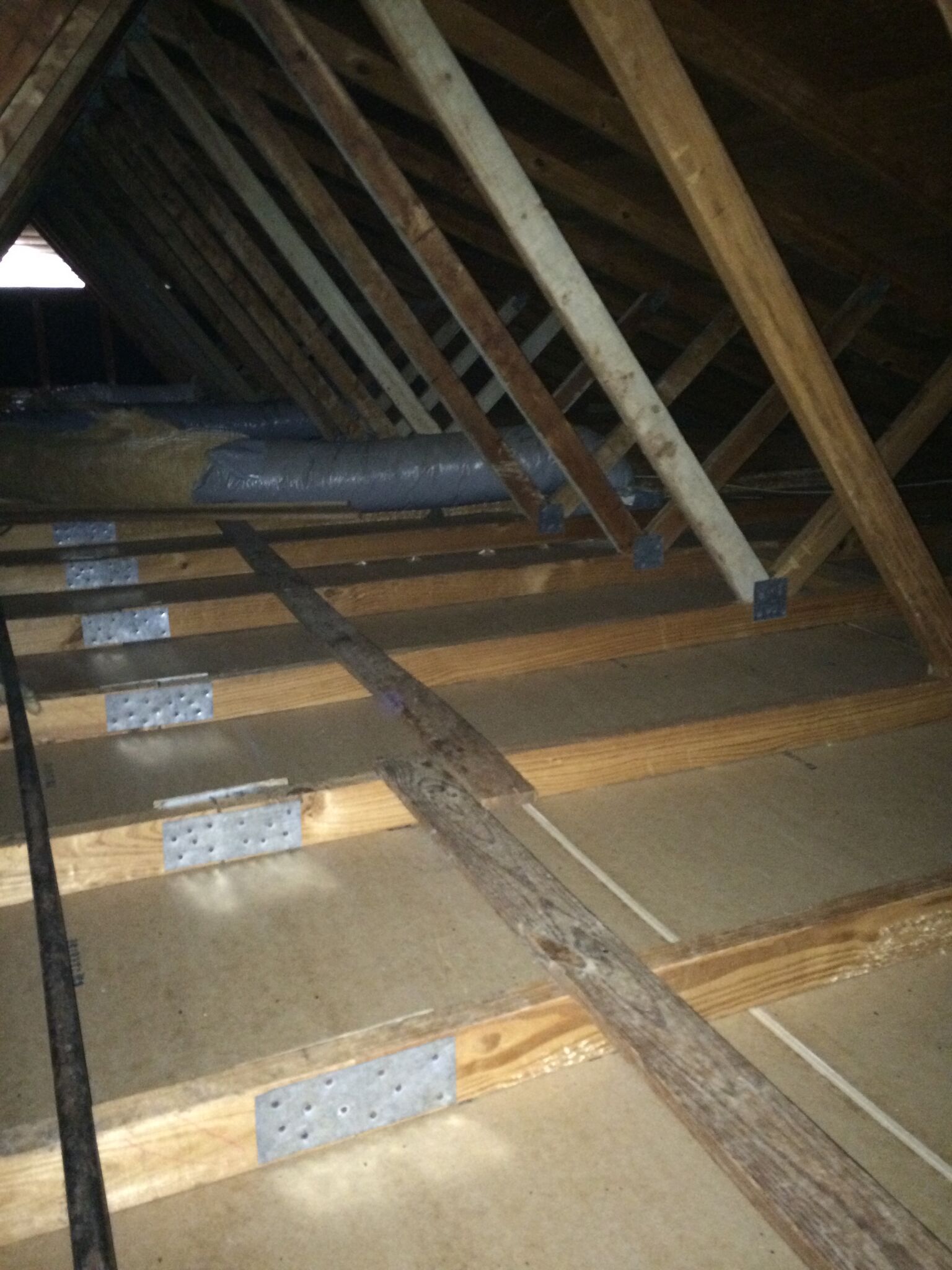 Interior of an attic with wooden rafters and beams. Some metal brackets are visible.