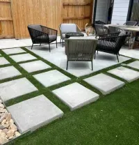 Modern backyard patio with gray paver stones, artificial grass, and outdoor furniture, bordered by a wooden fence.